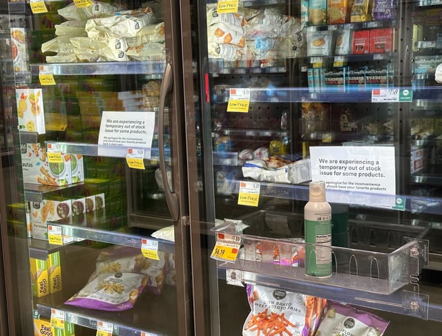 a photo of the frozen and refrigerated section at a local Whole Foods, with empty spaces, and signs warning of an out-of-stock issue.