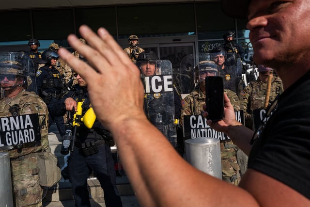 A person holds up their phone in front of the National Guard and police as they confront protesters following three days of clashes with police after a series of immigration raids on June 9, in Los Angeles.