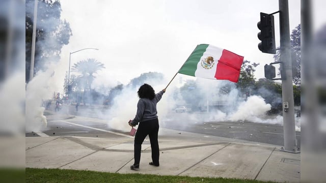 A woman waves a Mexican flag admist tear gas from law enforcement during a prote...