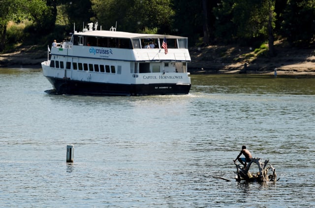 A man sits on a tangle of branches in the Sacramento River while staying cool during a heat wave in Sacramento, California, U.S. May 30, 2025.  REUTERS/Fred Greaves/File Photo