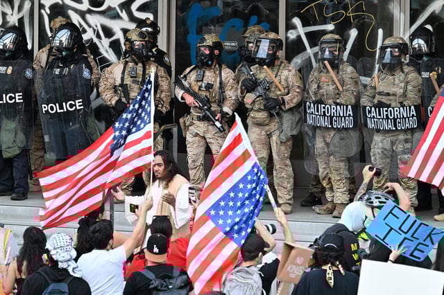 National Guard soldiers and federal police officers stand guard as a group of protestors wave US flags at the Federal Building in Los Angeles, California as protests continue in response to federal immigration operations on June 10, 2025.
