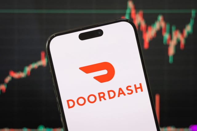 The logo of DoorDash, Inc. is displayed on a smartphone screen with a stock market chart in the background reflecting recent financial activity, on May 04, 2025.
