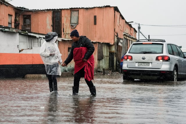 Residents walk across a flooded road following severe weather with heavy rain from a cold front in Masiphumelele, Cape Town, South Africa on May 20, 2025. REUTERS/Nic Bothma