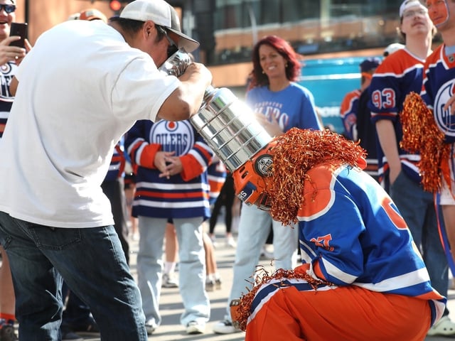 Edmonton Oilers' fan drinks a beer out of a Stanley Cup worn on the head of another fan, ahead of Game 3 of the Stanley Cup finals between the Oilers and Florida Panthers, from a watch party outside Rogers Place in downtown Edmonton, Monday, June 9, 2025. 