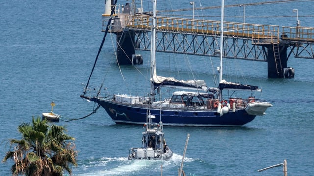 Ein Polizeiboot steuert auf eine Segelschiff in einem Hafen zu.