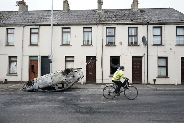 Spuren der Randale: Ein Mann fährt in Ballymena an einem ausgebrannten Auto vorbei.