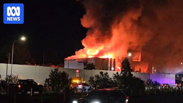 A large fire in a storage complex, cars in the foreground
