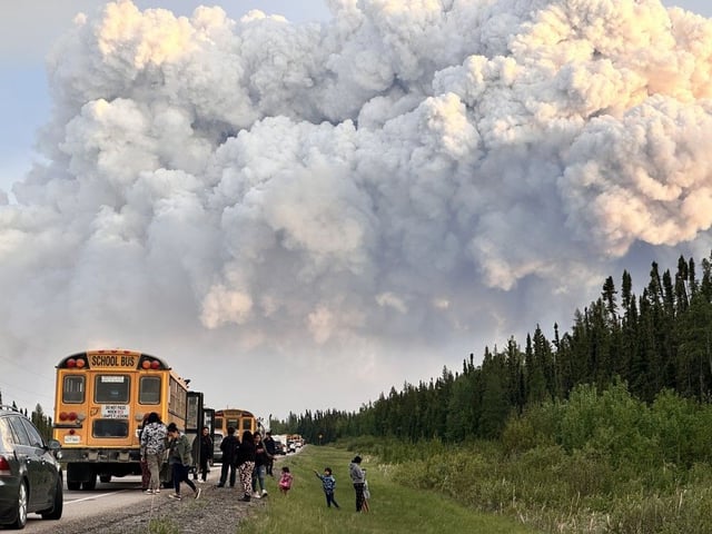 People stop along a highway as a large active wildfire fills the sky with smoke in the background in the La Ronge, Sask., area in an undated handout photo.