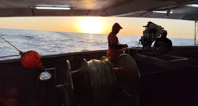 Marineros en la popa de un buque palangrero gallego en la puesta de sol.