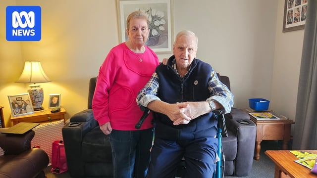 An elderly woman and man, who is in a wheelchair, in their living room.
