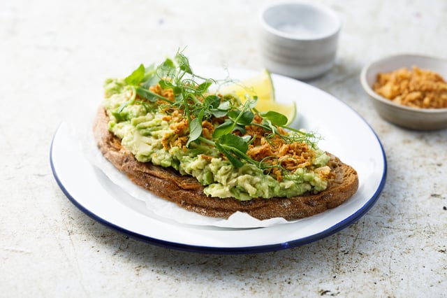 A stock image of a plate containing avocado on brown bread.