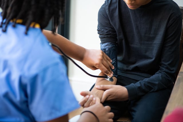 A nurse of takes the blood pressure of a teenage boy