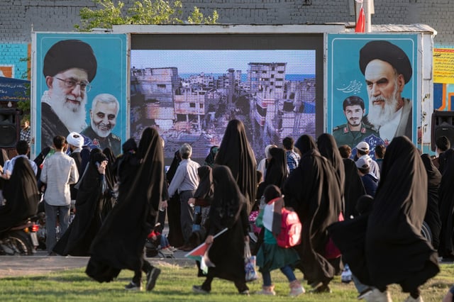 Protesters walk past a display featuring an image of Gaza and portraits of Iran's Supreme Leader, Ayatollah Ali Khamenei, late leader Ayatollah Ruhollah Khomeini, and former commander of the Islamic Revolutionary Guard Corps' Quds Force, Major General Qassem Soleimani, outside the holy mosque of Jamkaran near the holy city of Qom, Iran, on April 15, 2025, during a rally. 
