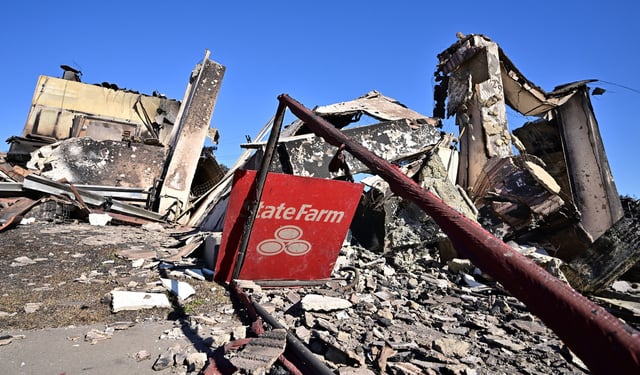 A State Farm insurance company sign sits amid the rubble of a building destroyed by the Palisades Fire on Sunset Boulevard in the Pacific Palisades neighborhood of Los Angeles on January 16, 2025.