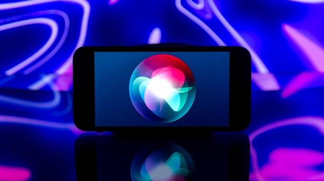 Ein Smartphone mit einem bunten abstrakten Design auf dem Bildschirm. Auf ihm ist das Siri-Logo zu sehen.