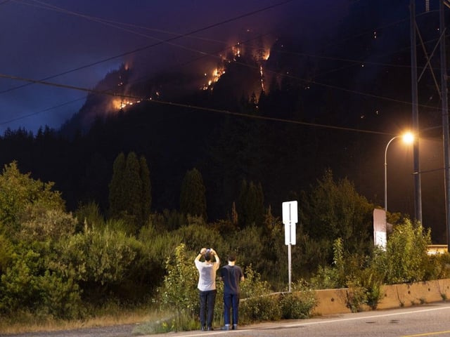 A couple take pictures of a wildfire as its spreads in Squamish, British Columbia on June 10, 2025. 