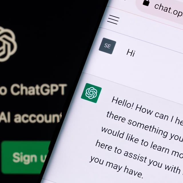 ChatGPT starting prompt seen on a phone screen, seen over a desktop display also displaying a ChatGPT webpage.