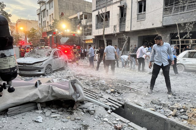 People and first-responders gather outside a building that was hit by an Israeli strike in Tehran on Friday. Israel hit about 100 targets in Iran,  including nuclear facilities and military command centers. (MEGHDAD MADADI/TASMIN NEWS/AFP/GETTY IMAGES)