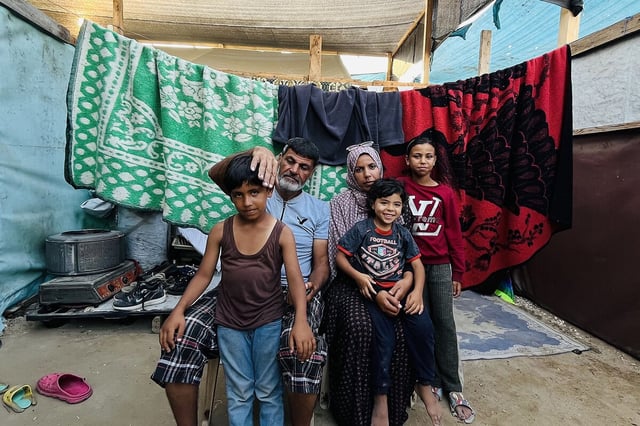 Mahmoud Hussein al-Haj Ahmed, a father of 12 who said he was nearly shot while attempting to receive aid, sits with family members in their tent in a displacement camp in central Gaza, June 11, 2025.