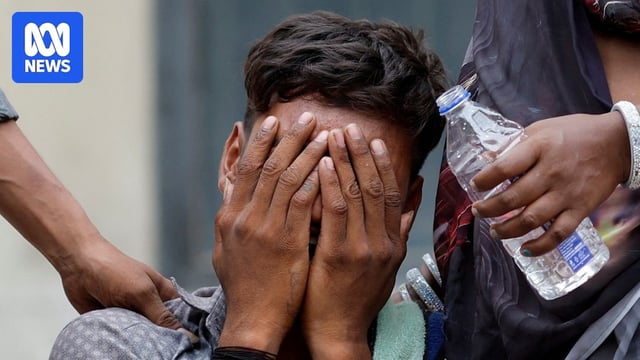 A distraught man puts his face in his hands as someone nearby puts an arm on his shoulder and other offers a bottle of water.