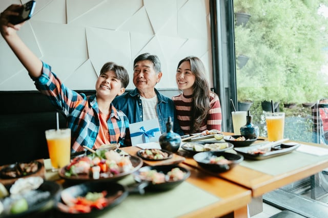A son takes a selfie of him, his dad and sister at a restaurant.