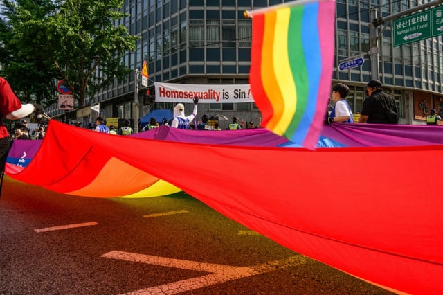 Participants in South Korea's annual Pride parade in Seoul carry a huge flag in support of LGBTQ rights past opponents holding a banner that reads "Homosexuality is sin!"