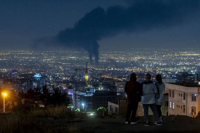 People gather on a hill to watch smoke rising in the distance from an Israeli airstrike in Tehran, Iran, on June 14, 2025.