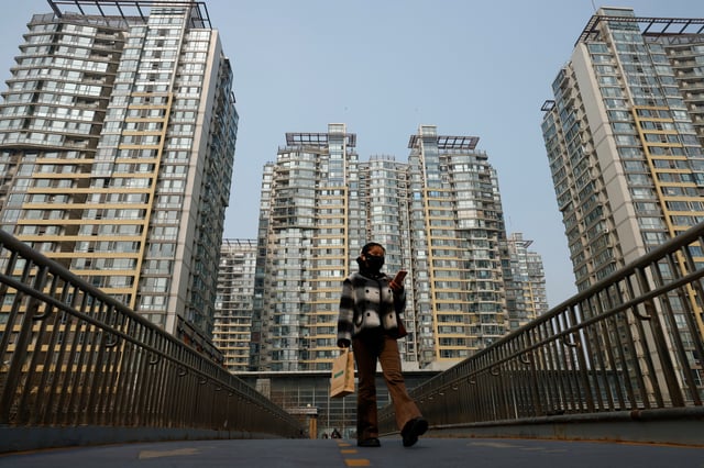 A woman walks on an overpass near residential buildings in Beijing, China, March 9, 2025. REUTERS/Tingshu Wang/File Photo