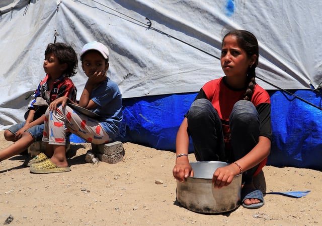 Displaced Palestinian children, one with an empty pot, sit while waiting to receive food from a charity kitchen, in Gaza City, June 3, 2025. REUTERS/Ebrahim Hajjaj/File Photo