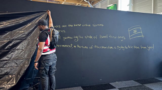 A security personnel works to hide a graffiti reading "Behind these walls are the best defense systems used by many countries. These systems are protecting the state of Israel these days. The French government, in the name of discrimination is trying to hide them from you!", on a panel of the Israel Aerospace Industries (IAI) Israeli Pavillon during the International Paris Air Show at the Le Bourget Airport on June 16, 2025. (Mathieu RABECHAULT/AFP)
