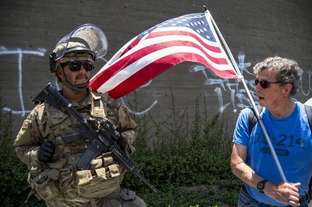 A protester holding an American flag speaks to a National Guard member in Los Angeles, Calif., on June 14, 2025.