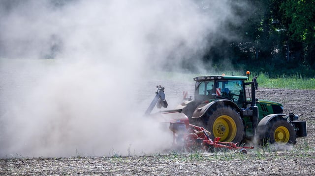 Ein Trecker fährt über ein Feld und zieht eine Staubwolke hinter sich her.