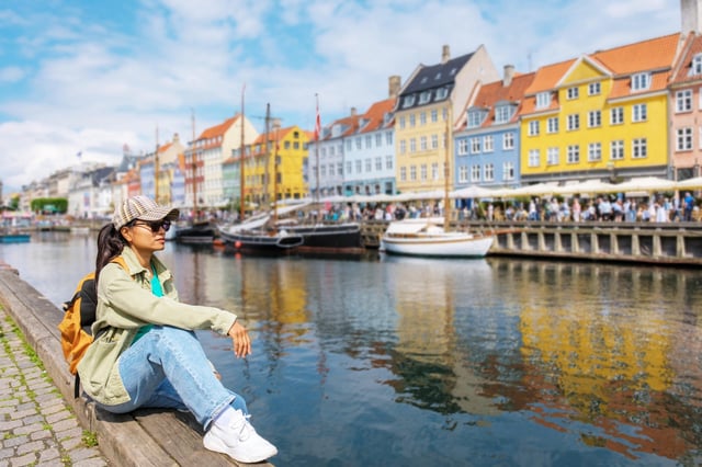 Relaxing by the serene waterfront in Nyhavn, Copenhagen, Denmark, a traveler enjoys the stunning view of vibrant buildings reflecting on the water. || Modellfreigabe vorhanden