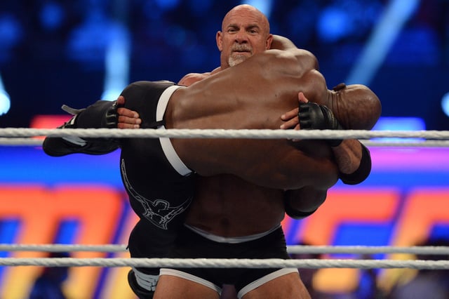 Goldberg (black trunks) with son Gage (street clothes) faces Bobby Lashley (black pants) with MVP (suit) for the WWE World Heavy Championship at SummerSlam 2021 at Allegiant Stadium.