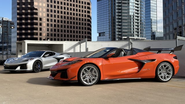 An orange Corvette ZR1X convertible and a silver ZR1X coupe parked on the top floor of a parking garage.