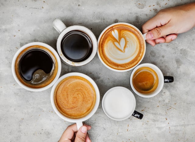 Two people hold coffee mugs that had been arranged among four other cups of the popular beverage.