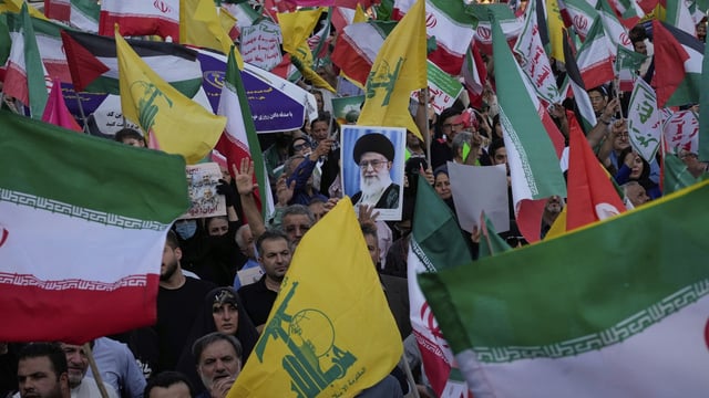 Demonstrators wave Iranian and Hezbollah flags as one holds up a poster of Iran's Supreme Leader Ayatollah Ali Khamenei 