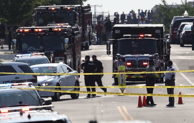 In this June 14, 2017 photo, investigators and emergency personnel gather adjacent to Eugene Simpson Field, the site where a gunman opened fire in Alexandria, Virginia.
