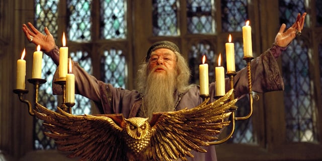 Dumbledore (Michael Gambon) giving a speech while spreading his arms behind a podium with an owl on it in Harry Potter and the Goblet of Fire.