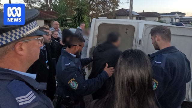 A man being led by multiple police officers into the back of a paddy wagon.