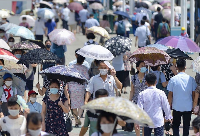 People wearing masks for protection against the coronavirus walk in Pyongyang amid the scorching summer heat on July 20, 2021.