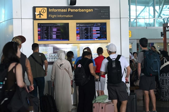 Des voyageurs regardent les tableaux d'information affichant les vols annulés après l'éruption du mont Lewotobi Laki-Laki, à l'aéroport international Ngurah Rai de Tuban, près de Denpasar, sur l'île touristique de Bali, le 18 juin 2025 en Indonésie