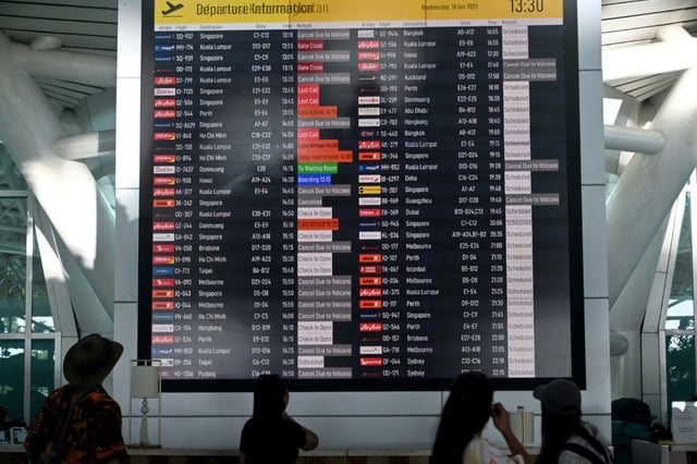 Des voyageurs consultent un tableau d'information affichant les vols annulés après l'éruption du mont Lewotobi Laki-Laki, à l'aéroport international Ngurah Rai de Tuban, près de Denpasar, sur l'île touristique de Bali, le 18 juin 2025 en Indonésie