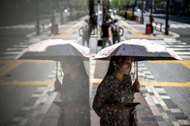 Une passante utilise un parapluie pour se protéger du soleil dans une rue du quartier de Yurakucho à Tokyo où les températures ont dépassé les 34°C, le 18 juin 2025