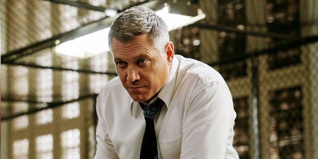 holt mccallany as Bill Tench in Mindhunter leaning over a desk