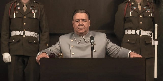 Russell Crowe sitting at a podium with two officers behind him in Nuremberg