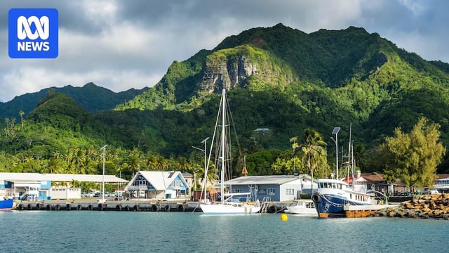 A view from the ocean of a small town, boats at dock and forest-covered hills.