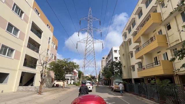 the rider can be seen navigating a stretch of road where an imposing high-tension (HT) transmission tower obstructs the path.