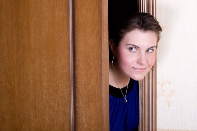 A stock image of a woman sticking her head out from behind a door.