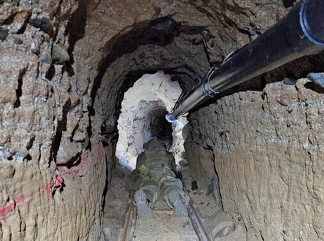 An uncompleted smuggling tunnel between Tijuana and Otay Mesa uncovered by the U.S. Border Patrol in San Diego. A Tunnel Team agent crawls along the track. (U.S. Border Patrol)